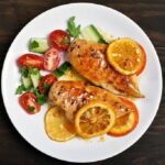 1. Introducción al Pollo a la Naranja al Horno El pollo a la naranja al horno es una receta deliciosa que combina la suavidad de la carne de pollo con el sabor fresco, dulce y ligeramente ácido de la naranja. Este plato es muy popular en muchas cocinas del mundo porque logra un equilibrio perfecto entre sabores naturales, aromas cítricos y una textura jugosa que se obtiene gracias a la cocción lenta en el horno. La naranja aporta un toque especial al pollo, creando una salsa natural que impregna cada pieza de carne con un sabor intenso y refrescante. Además, al cocinarse en el horno, el pollo adquiere una superficie dorada y ligeramente caramelizada, mientras que por dentro permanece tierno y jugoso. Esta receta es ideal para diferentes ocasiones. Puede servirse como plato principal en una comida familiar, en una cena especial o incluso en reuniones con amigos. Su preparación no es complicada y no requiere ingredientes difíciles de encontrar, lo que la convierte en una opción perfecta para quienes desean preparar un plato elegante sin pasar demasiado tiempo en la cocina. Otro aspecto destacado del pollo a la naranja al horno es su valor nutricional. El pollo es una fuente excelente de proteínas, mientras que la naranja aporta vitamina C, antioxidantes y un aroma natural que mejora el sabor del plato sin necesidad de usar demasiados condimentos artificiales. Además, esta receta se puede acompañar fácilmente con diferentes guarniciones como arroz blanco, puré de patatas, verduras asadas o ensalada fresca. Gracias a su versatilidad, el pollo a la naranja al horno se adapta a muchos estilos de cocina y preferencias gastronómicas. Si buscas una receta sabrosa, saludable y fácil de preparar, esta opción será una excelente elección. A continuación, veremos los ingredientes necesarios y el proceso paso a paso para preparar este delicioso plato. 2. Ingredientes para preparar Pollo a la Naranja al Horno Para preparar un delicioso pollo a la naranja al horno, es importante utilizar ingredientes frescos y de buena calidad. Esto garantizará un sabor más intenso y una mejor textura en el resultado final. Ingredientes principales 1 pollo entero troceado o 4 muslos de pollo 3 naranjas grandes y jugosas 3 dientes de ajo 1 cebolla mediana 2 cucharadas de miel 2 cucharadas de salsa de soja 3 cucharadas de aceite de oliva 1 cucharadita de pimienta negra 1 cucharadita de sal 1 cucharadita de pimentón dulce 1 ramita de romero o tomillo (opcional) Ingredientes opcionales para intensificar el sabor 1 cucharadita de jengibre rallado 1 cucharada de mostaza 1 cucharada de azúcar moreno ralladura de naranja Guarniciones recomendadas Aunque el pollo a la naranja al horno puede servirse solo, también combina muy bien con: arroz blanco patatas al horno verduras asadas ensalada fresca cous cous Estos acompañamientos ayudan a equilibrar el plato y permiten disfrutar mejor de la deliciosa salsa de naranja que se forma durante la cocción. 3. Preparación paso a paso del Pollo a la Naranja al Horno Preparar esta receta es bastante sencillo si se siguen los pasos correctamente. A continuación se explica el proceso completo para obtener un pollo jugoso y lleno de sabor. Paso 1: Preparar el horno Precalienta el horno a 180 °C durante unos 10 minutos antes de empezar la cocción. Esto permitirá que el pollo se cocine de manera uniforme desde el principio. Paso 2: Preparar la marinada de naranja Exprime el jugo de dos naranjas en un recipiente grande. Luego añade: la miel la salsa de soja el aceite de oliva el ajo picado la pimienta el pimentón dulce el jengibre (opcional) Mezcla todos los ingredientes hasta obtener una salsa homogénea. Esta marinada será la base del sabor del plato. Paso 3: Marinar el pollo Coloca las piezas de pollo en un recipiente grande o en una bolsa de cocina. Vierte la marinada sobre el pollo y asegúrate de que todas las piezas queden bien cubiertas. Para lograr un sabor más intenso, deja marinar el pollo durante 30 minutos a 2 horas en el refrigerador. Cuanto más tiempo repose, mejor absorberá los sabores. Paso 4: Preparar la bandeja de horno Corta la cebolla en rodajas y colócala en el fondo de una bandeja para horno. Esto ayudará a aromatizar el pollo durante la cocción. Coloca las piezas de pollo encima de la cebolla y vierte parte de la marinada restante sobre ellas. Corta la tercera naranja en rodajas y distribúyelas alrededor del pollo. Paso 5: Hornear el pollo Introduce la bandeja en el horno precalentado y cocina durante 40 a 50 minutos. A mitad de la cocción, abre el horno y utiliza una cuchara para rociar el pollo con la salsa que se está formando en la bandeja. Esto ayudará a mantener la carne jugosa y a intensificar el sabor. Si deseas que el pollo tenga una piel más dorada, puedes aumentar la temperatura a 200 °C durante los últimos 10 minutos de cocción. Paso 6: Comprobar la cocción El pollo estará listo cuando la carne esté bien cocida y la superficie tenga un color dorado. Si al pinchar la carne sale un jugo claro, significa que está perfectamente cocido. Una vez listo, retira la bandeja del horno y deja reposar el pollo durante unos 5 minutos antes de servir. 4. Consejos para disfrutar mejor el Pollo a la Naranja al Horno Para disfrutar al máximo de esta receta, es recomendable tener en cuenta algunos consejos que mejorarán la experiencia gastronómica. Usar naranjas frescas El sabor del plato depende en gran parte del jugo de naranja. Por eso, es mejor utilizar naranjas naturales recién exprimidas en lugar de jugo procesado. No cocinar el pollo demasiado tiempo Si el pollo permanece demasiado tiempo en el horno, puede volverse seco. Lo ideal es controlar la cocción y retirar el pollo cuando esté dorado y jugoso. Aprovechar la salsa La salsa que queda en la bandeja es muy sabrosa. Puedes usarla para: rociar el pollo al servir mezclar con arroz acompañar patatas o verduras Añadir hierbas aromáticas Hierbas como el romero, tomillo o perejil pueden aportar un aroma extra al plato y hacerlo aún más apetitoso. Servir inmediatamente El pollo a la naranja al horno se disfruta mucho más cuando está recién hecho. Servirlo caliente permite apreciar mejor la textura jugosa del pollo y el aroma cítrico de la salsa. Conclusión El pollo a la naranja al horno es una receta sencilla, deliciosa y perfecta para cualquier ocasión. Gracias a la combinación del pollo con el jugo natural de naranja, este plato logra un sabor equilibrado entre dulce, ácido y salado que resulta irresistible. Además, su preparación es fácil y no requiere técnicas complicadas, por lo que cualquier persona puede cocinarlo en casa con excelentes resultados. Con ingredientes simples y un proceso claro, es posible preparar un plato que parece digno de un restaurante. Si te gusta experimentar con recetas de pollo llenas de sabor, el pollo a la naranja al horno es definitivamente una opción que vale la pena probar. Una vez que lo prepares, seguramente se convertirá en una de tus recetas favoritas para compartir con familia y amigos.